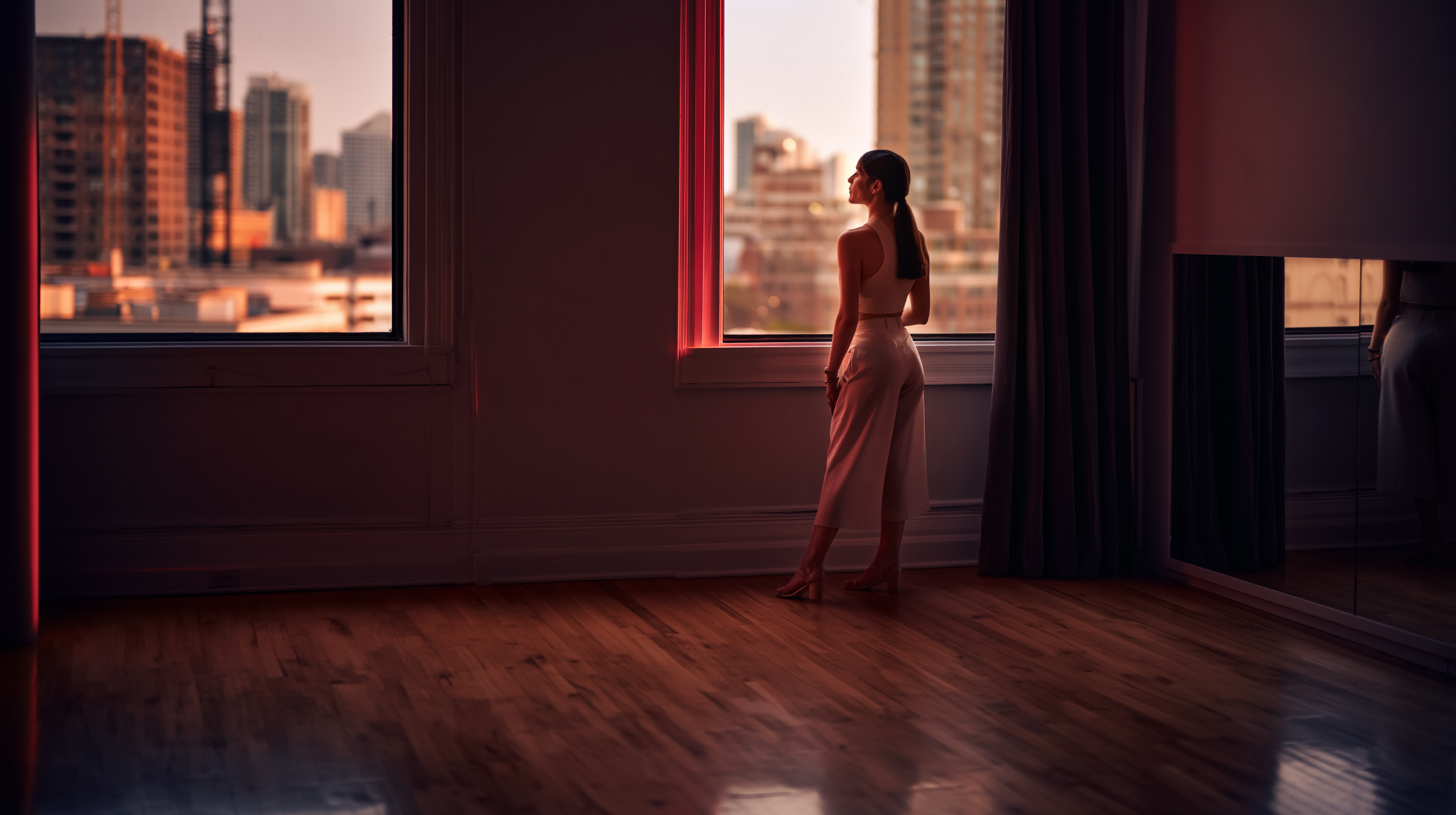 Founder standing in an empty Latin dance studio, looking out a tall window at the city