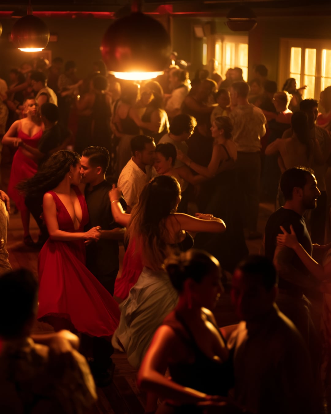 Packed Latin dance social with couples dancing salsa under warm pendant lights