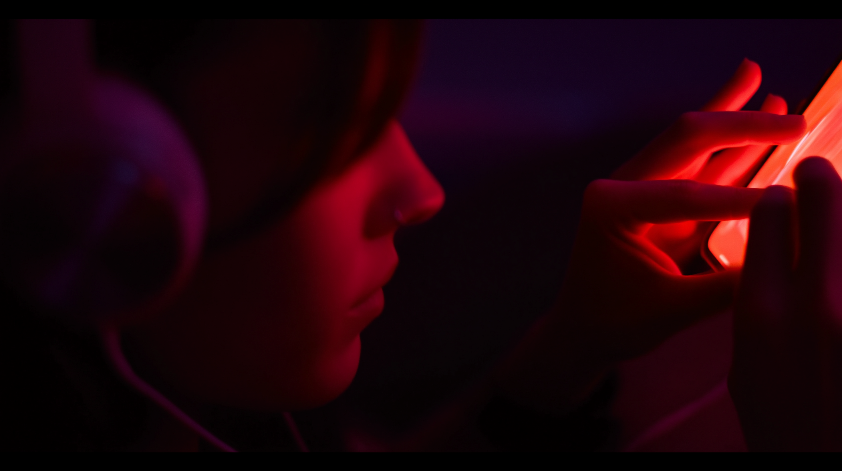 Close-up of fingertips tapping on a glowing iPhone screen in low light, headphones visible